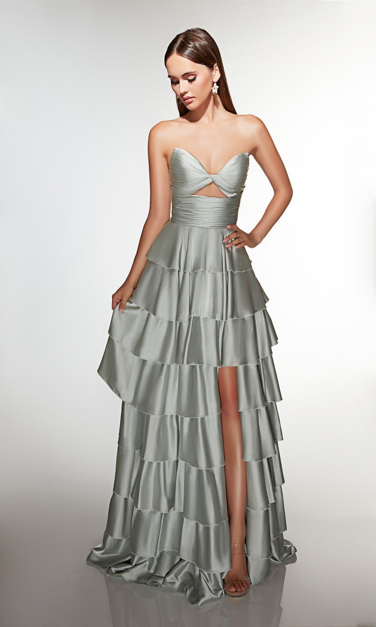A woman wearing the Alyce 61987 long prom dress in celadon, featuring a strapless ruffled design with a front slit, stands against a plain white background.